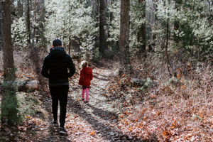 A man and a small girl walk on a path through woods