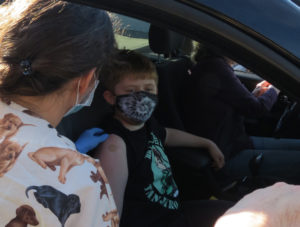 Nurse vaccinates a boy sitting in a car